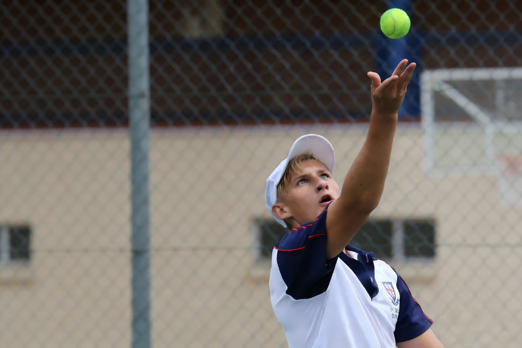 Boy serving tennis on outdoor hard court, using our sports court surface solutions